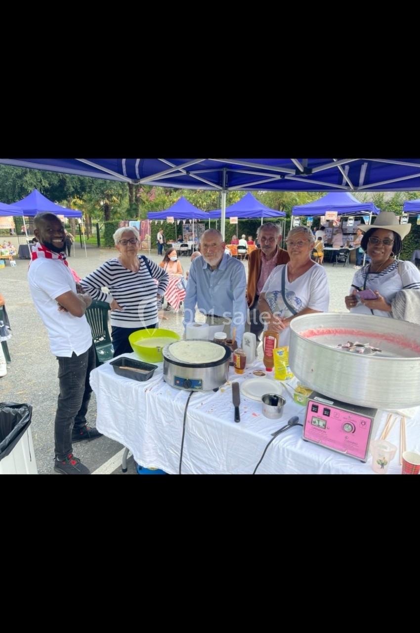 Des personnes souriantes rassemblées autour d'un stand de nourriture en plein air, sous des parasols bleus.