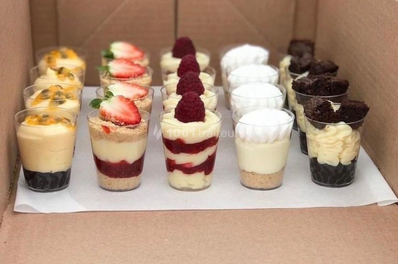 Assortiment de verrines sucrées avec fruits, mousse et gâteaux, disposées dans une boîte en carton.