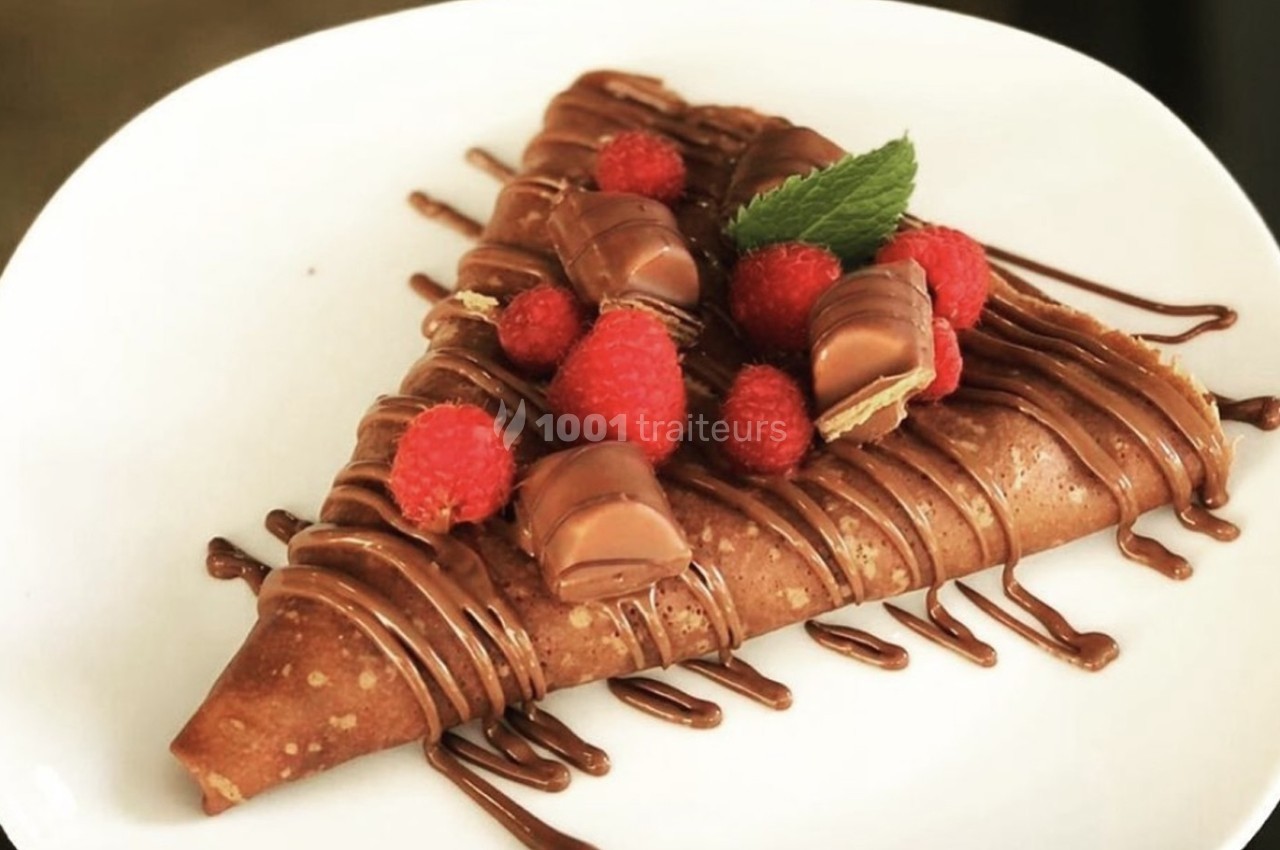 Crêpe garnie de framboises, morceaux de chocolat et nappée de sauce chocolat, servie sur une assiette blanche.