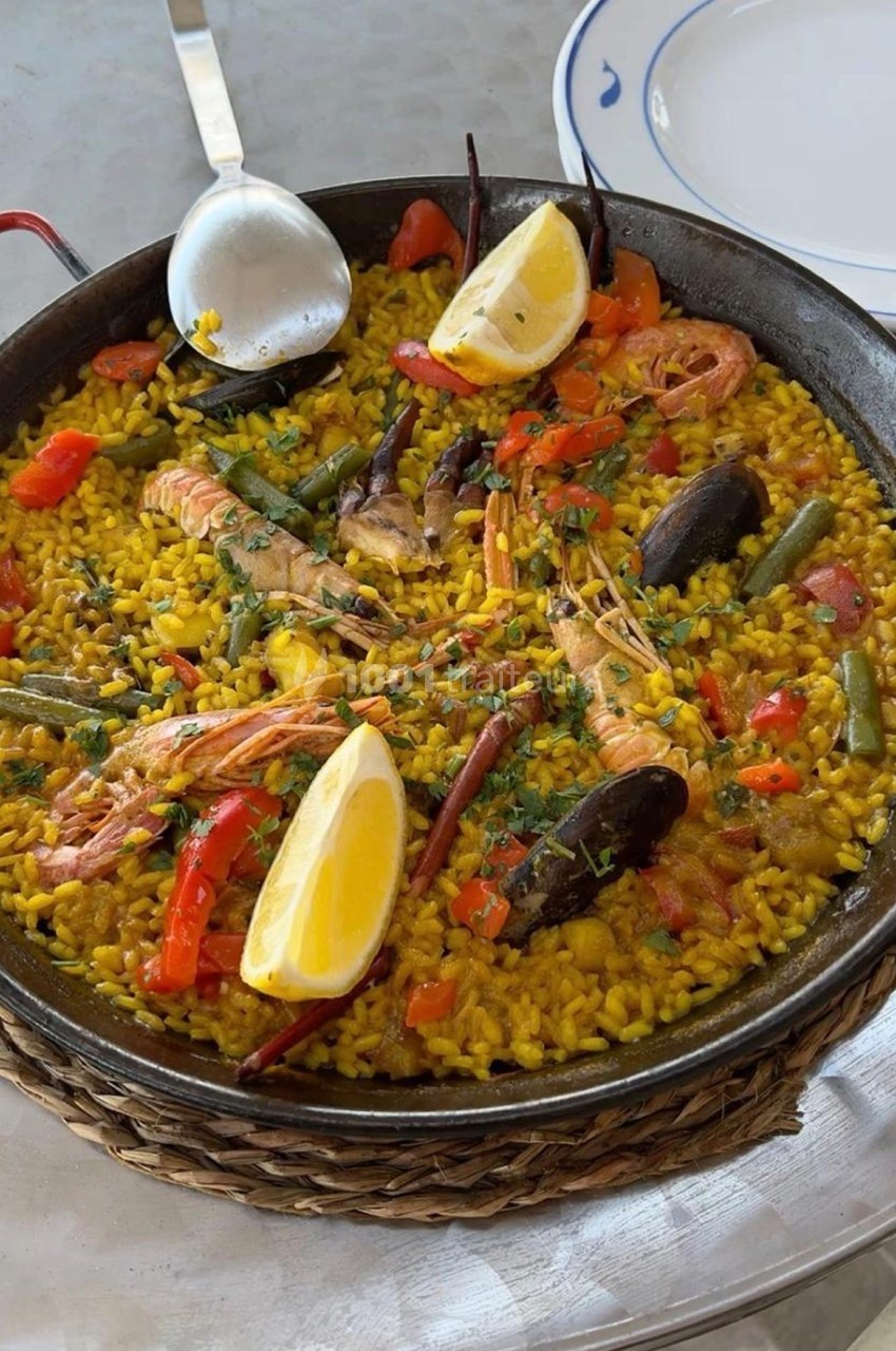 Plat de paella aux fruits de mer avec crevettes, moules, légumes et quartiers de citron, servi dans une poêle.