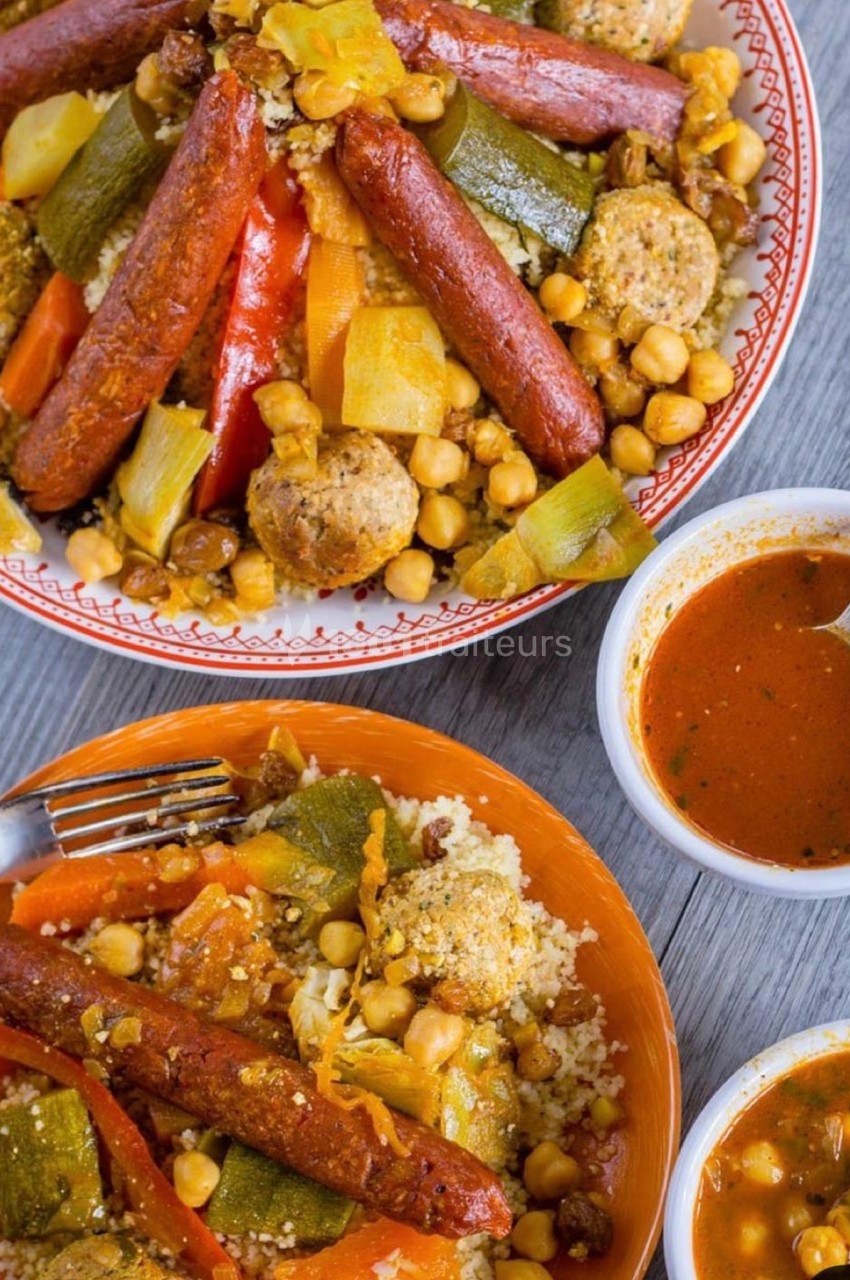Assiette de couscous garni de légumes, merguez, boulettes et pois chiches, accompagné de sauce rouge.