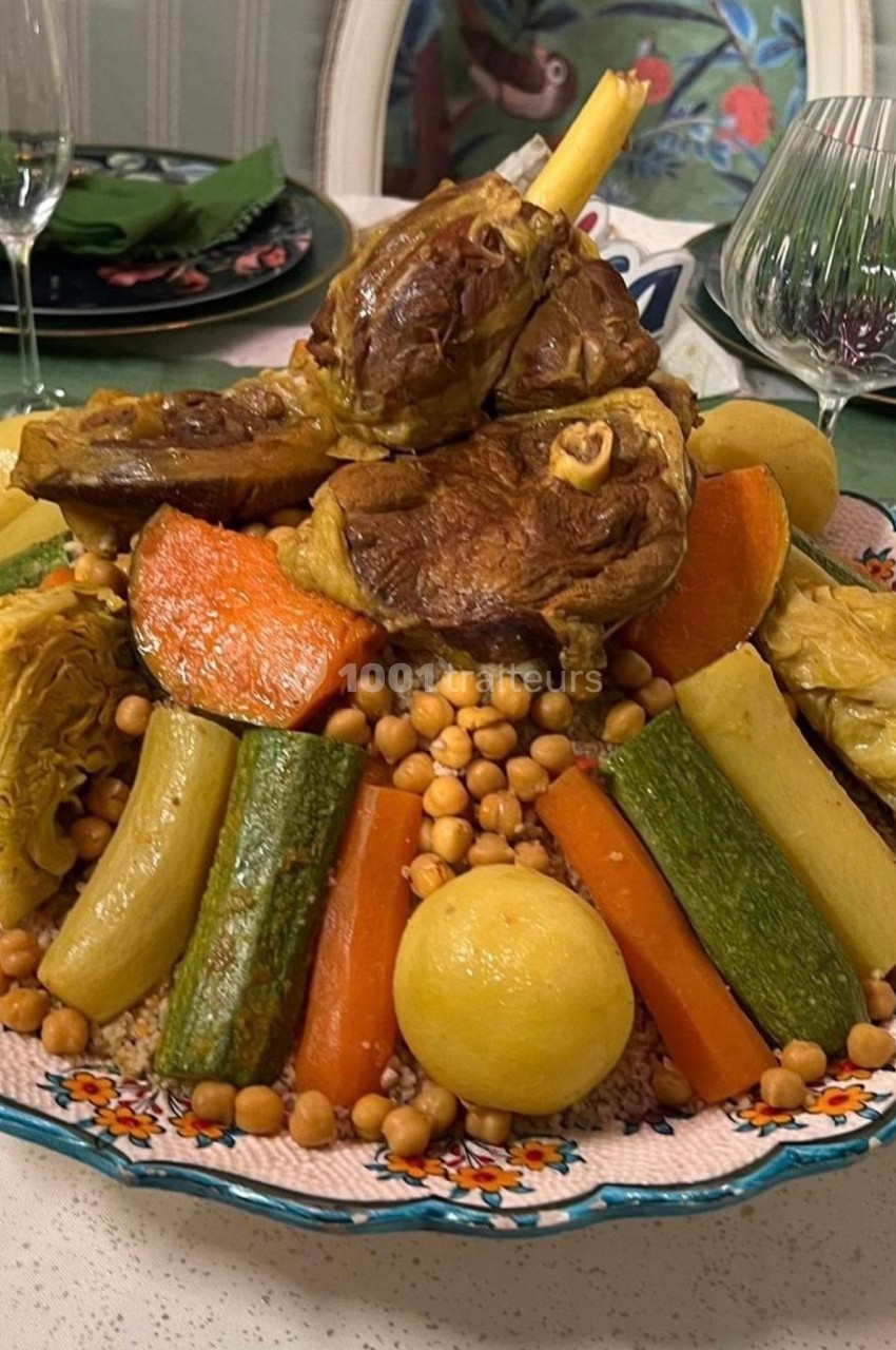 Plat de couscous garni de légumes variés, pois chiches et morceaux de viande, servi dans un grand plat décoré.