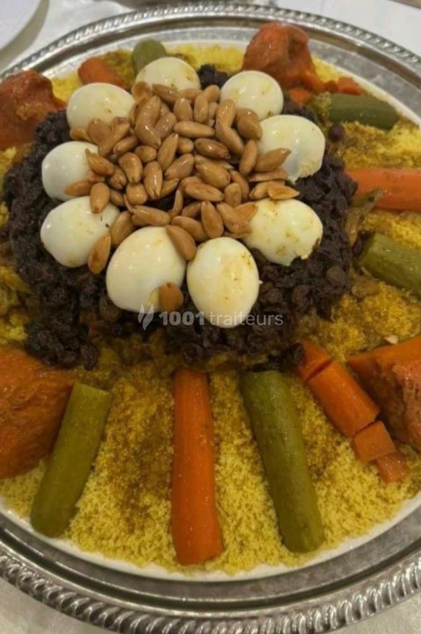Plat de couscous garni de légumes, œufs de caille, raisins secs, amandes et morceaux de viande, présenté sur un plateau.