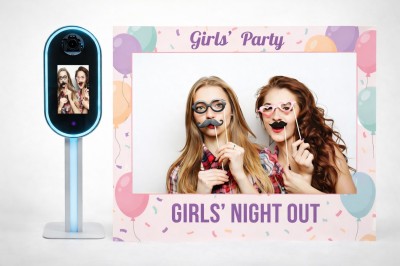 Un couple souriant en tenue de mariage pose devant une borne photo interactive lors d'une réception en extérieur.