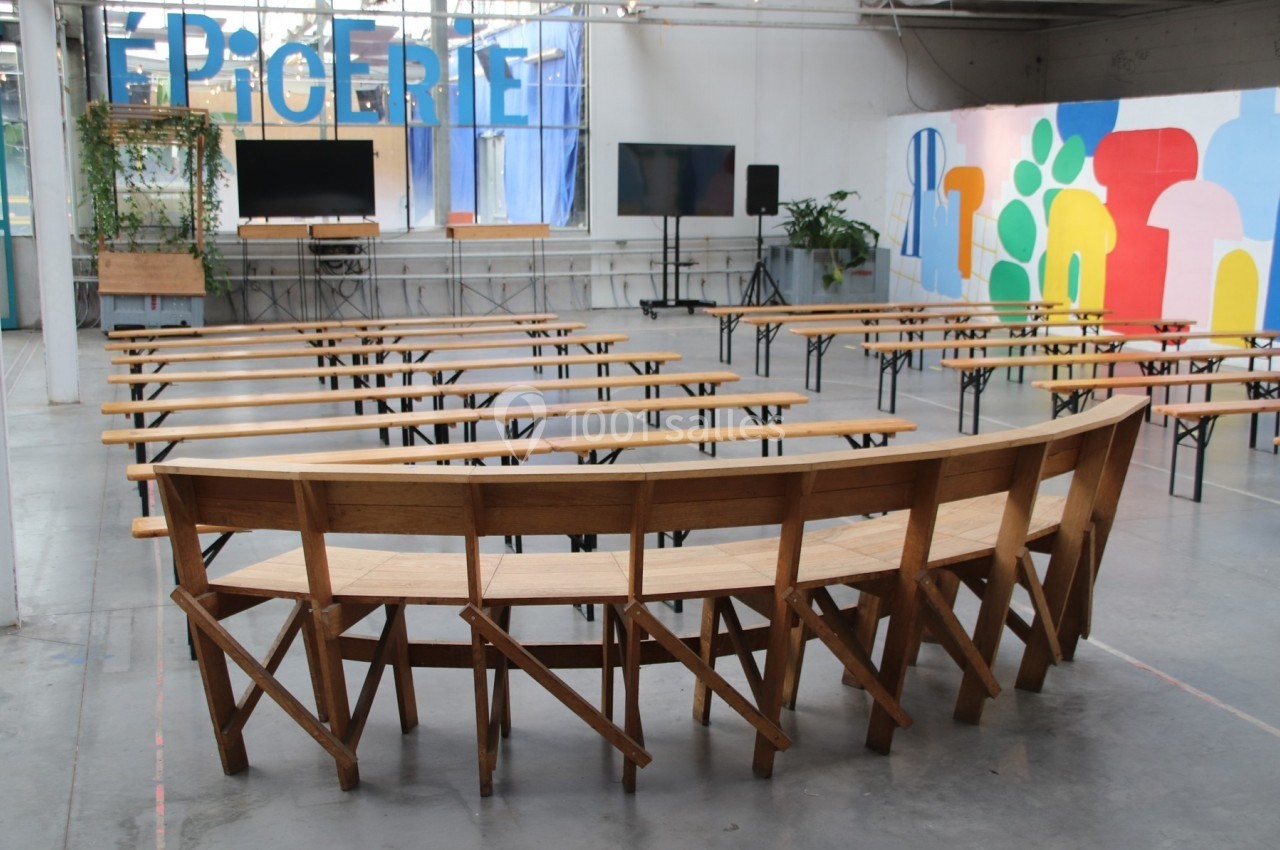 Salle lumineuse avec bancs en bois disposés en arc de cercle, écrans et décorations colorées en arrière-plan.