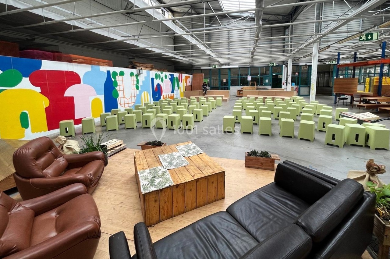Salle spacieuse avec des sièges verts alignés, un coin salon en cuir et une fresque colorée sur le mur.