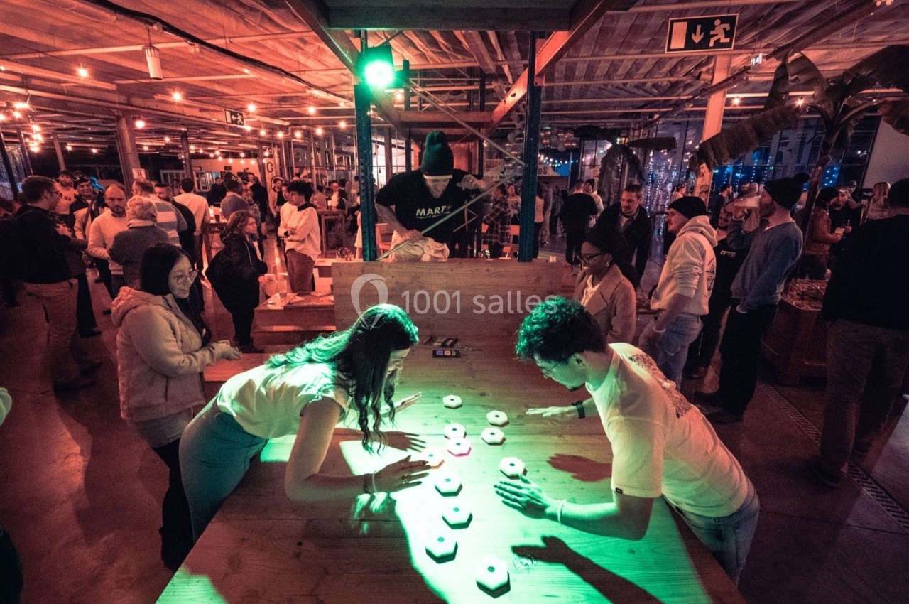 Des personnes jouent à un jeu interactif lumineux sur une table en bois dans un espace intérieur animé et éclairé.