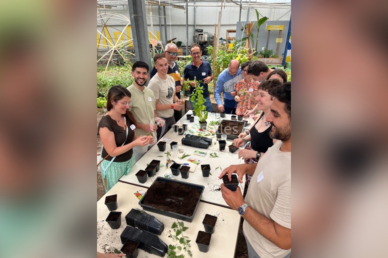 Des personnes participent à un atelier de jardinage dans une serre, préparant des semis autour d'une table.