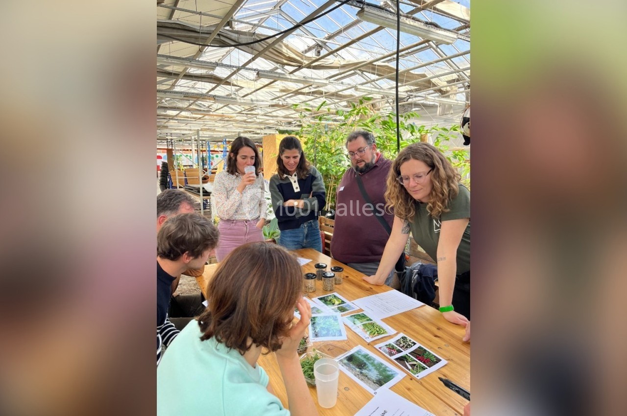 Un groupe de personnes observe et discute autour de documents et d'échantillons sur une table en bois dans une serre.