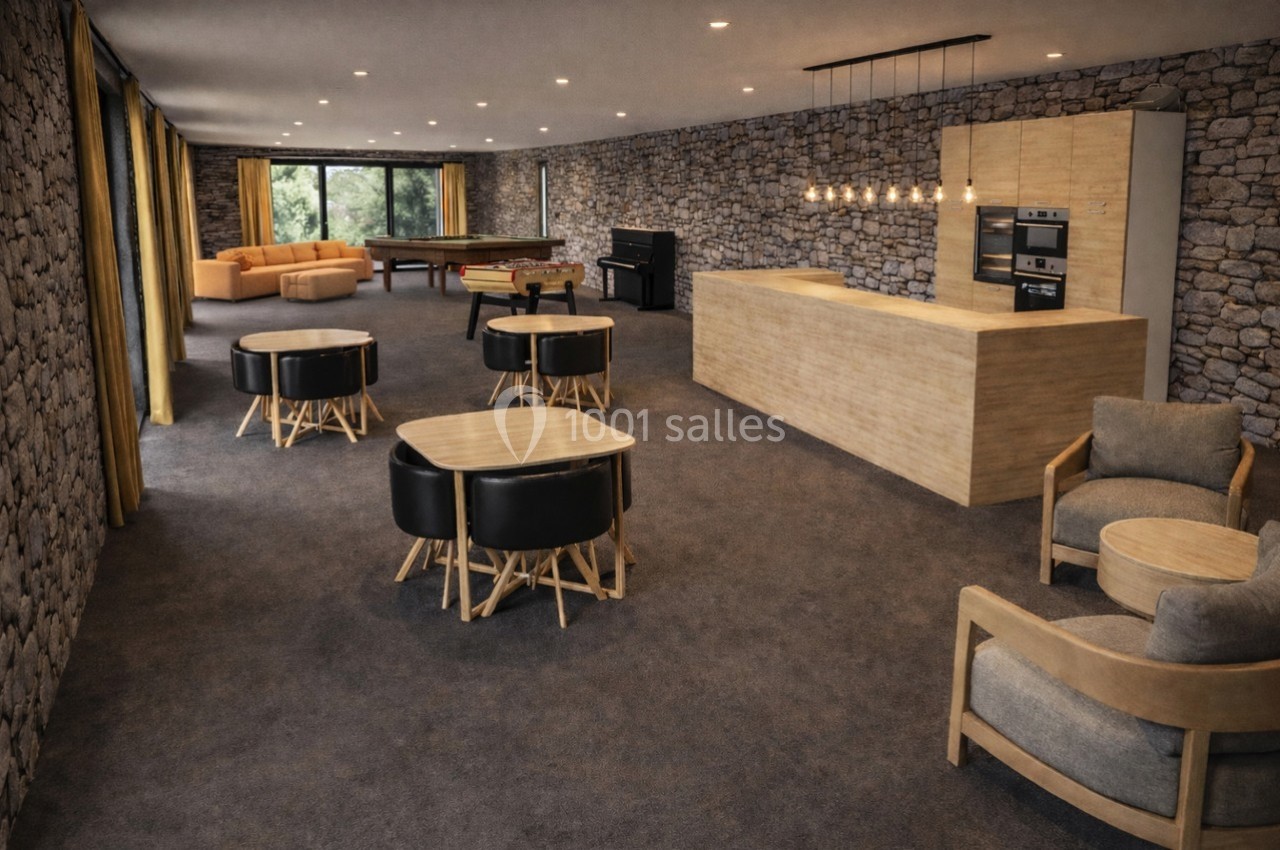 Salle spacieuse avec murs en pierre, cuisine ouverte, tables, fauteuils, billard, piano et grandes baies vitrées.