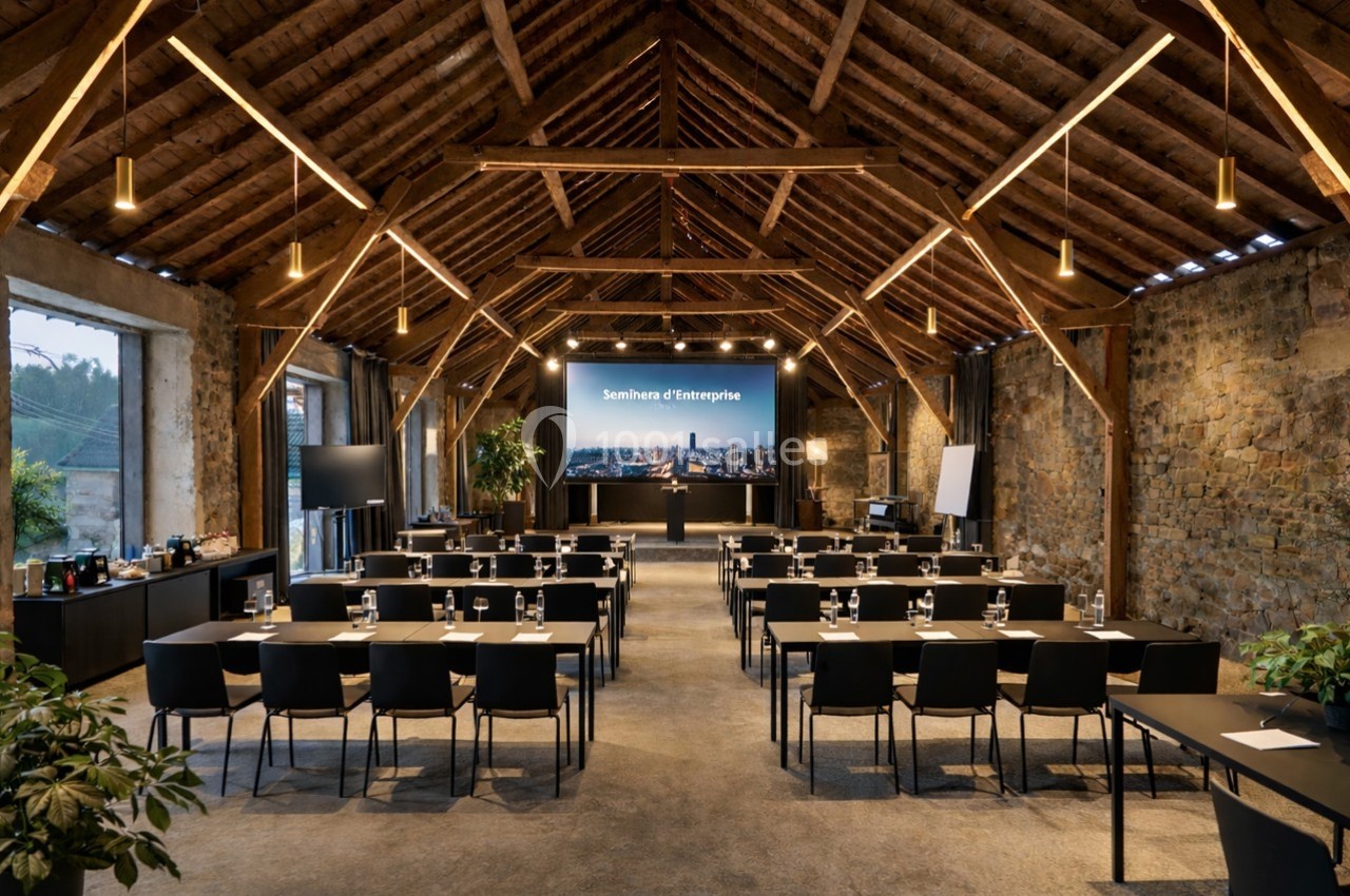 Salle de séminaire avec plafond en bois, tables alignées, chaises noires et écran de présentation allumé.