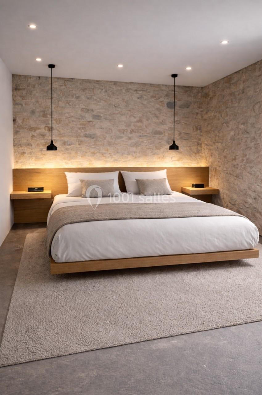 Lit double avec tête de lit en bois, éclairage intégré, murs en pierre et suspensions noires dans une chambre moderne.