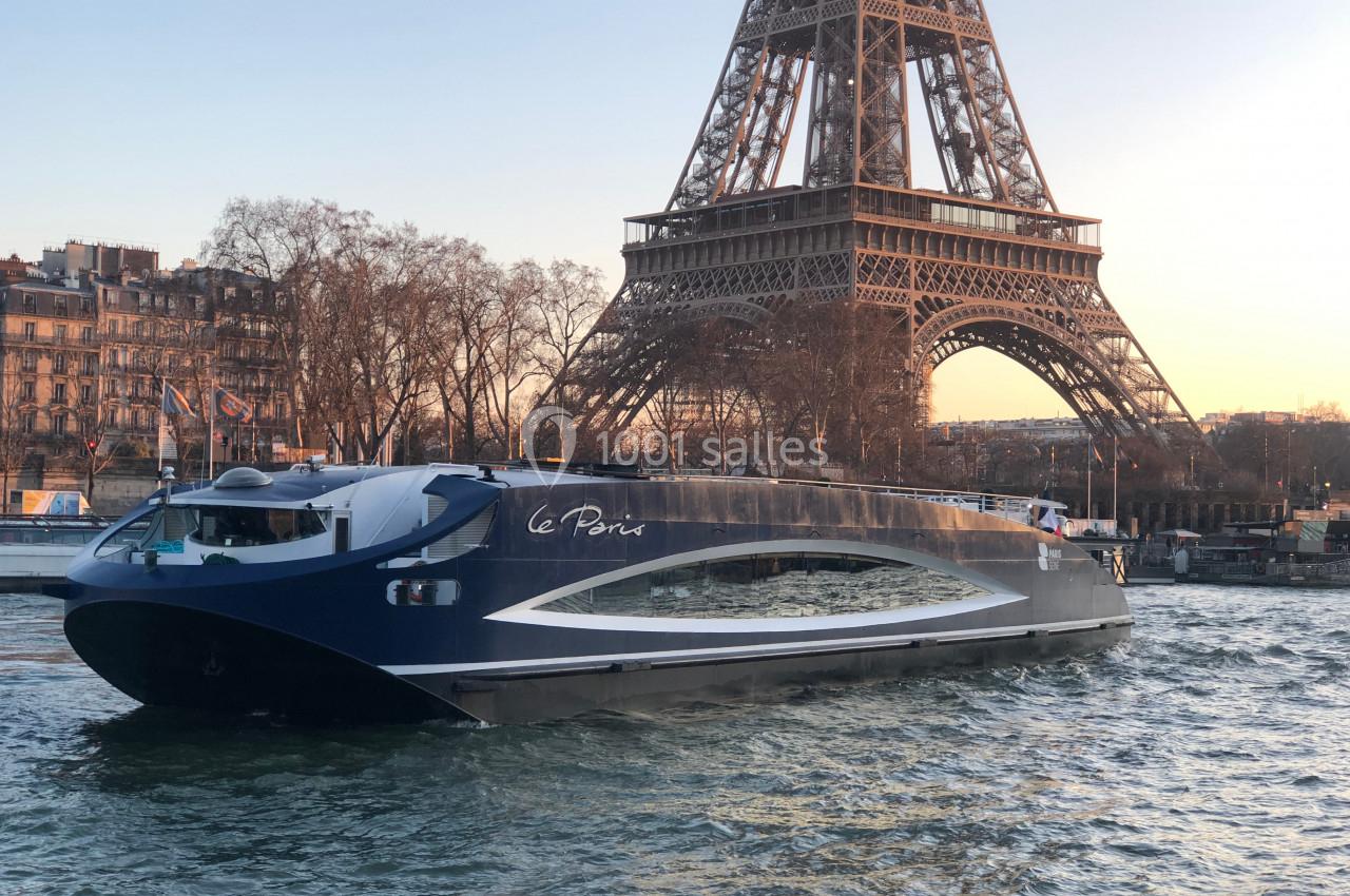Bateau moderne naviguant sur la Seine devant la tour Eiffel au coucher du soleil.