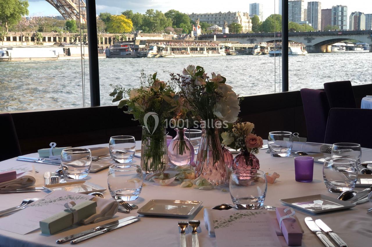 Table élégamment dressée avec des fleurs au centre, vue sur la Seine, la tour Eiffel et des bâtiments en arrière-plan.