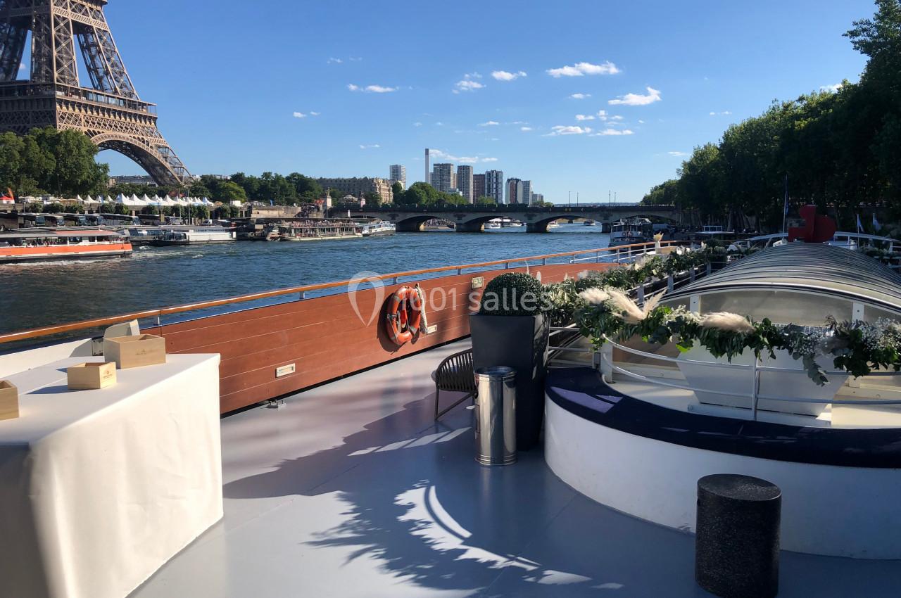Vue depuis le pont d'un bateau sur la Seine, avec la tour Eiffel, un pont et des bâtiments en arrière-plan.