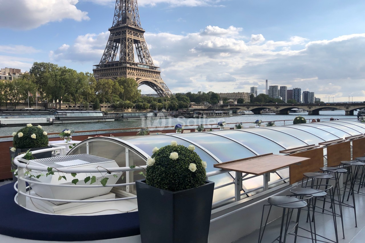 Vue depuis le pont d'un bateau sur la Seine, avec la tour Eiffel en arrière-plan et des tables aménagées.