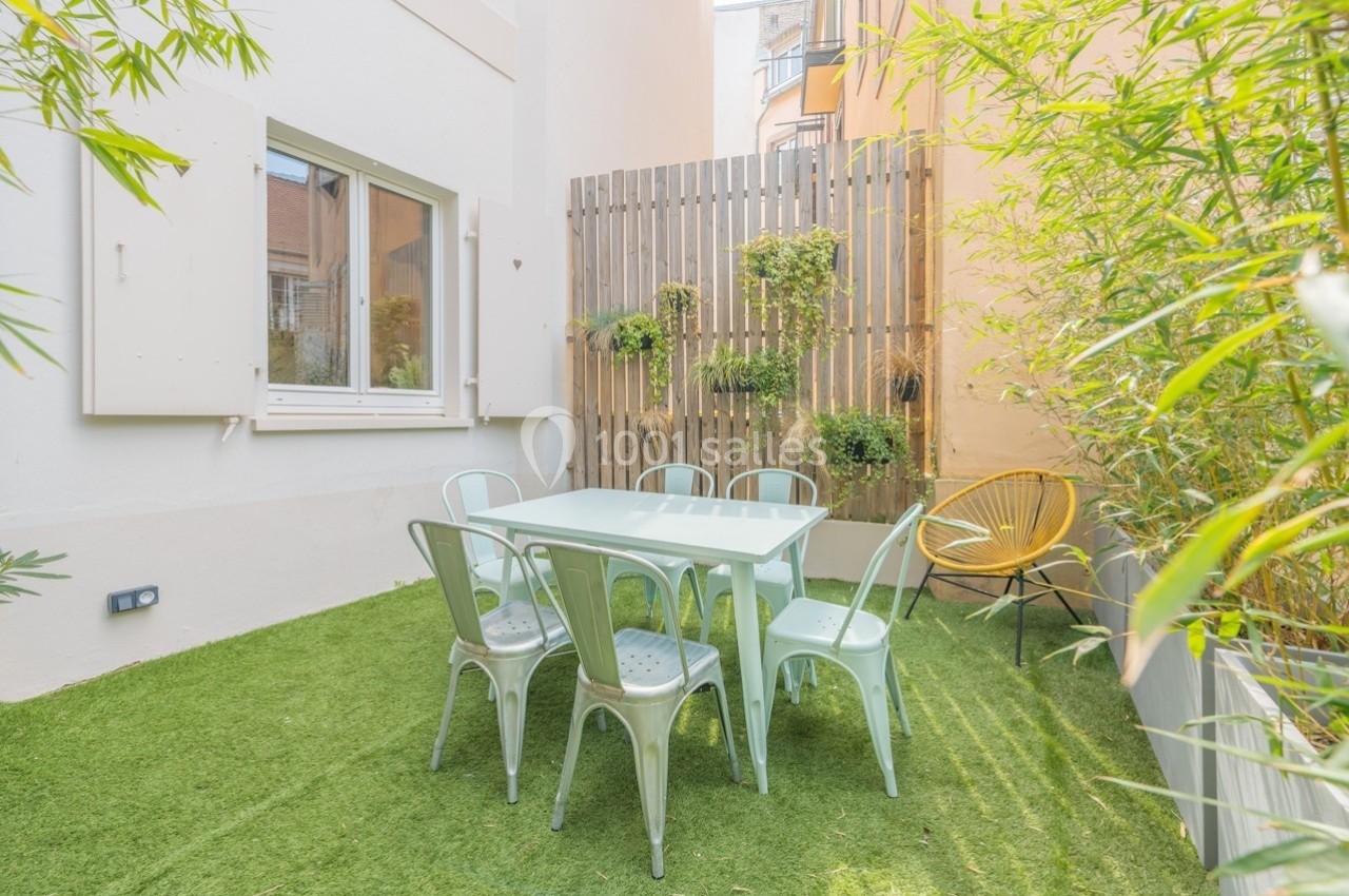 Terrasse extérieure avec table, chaises métalliques, mur végétalisé et sol en gazon synthétique, entourée de bambous.