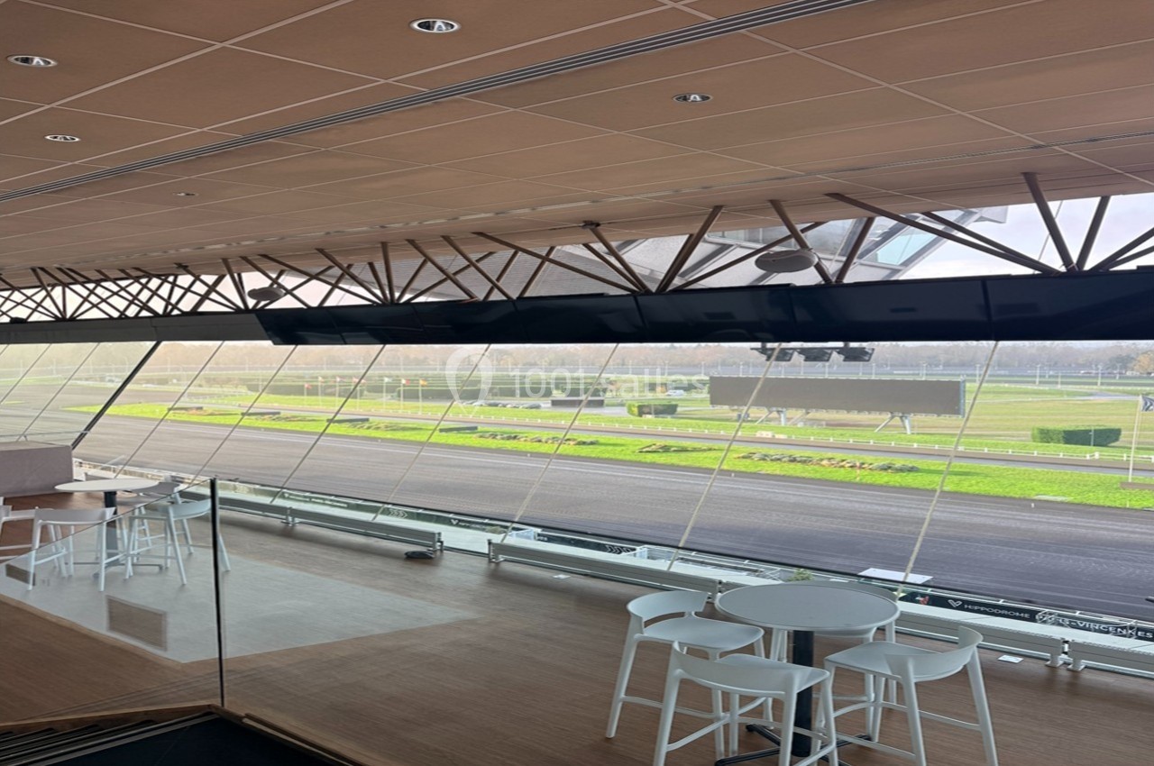 Vue intérieure d'une salle avec baies vitrées donnant sur une piste extérieure et des espaces verts.