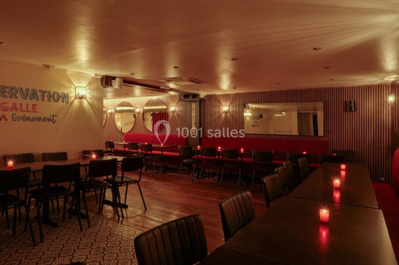 Salle de restaurant avec tables noires, banquettes rouges, éclairage tamisé et bougies sur les tables.