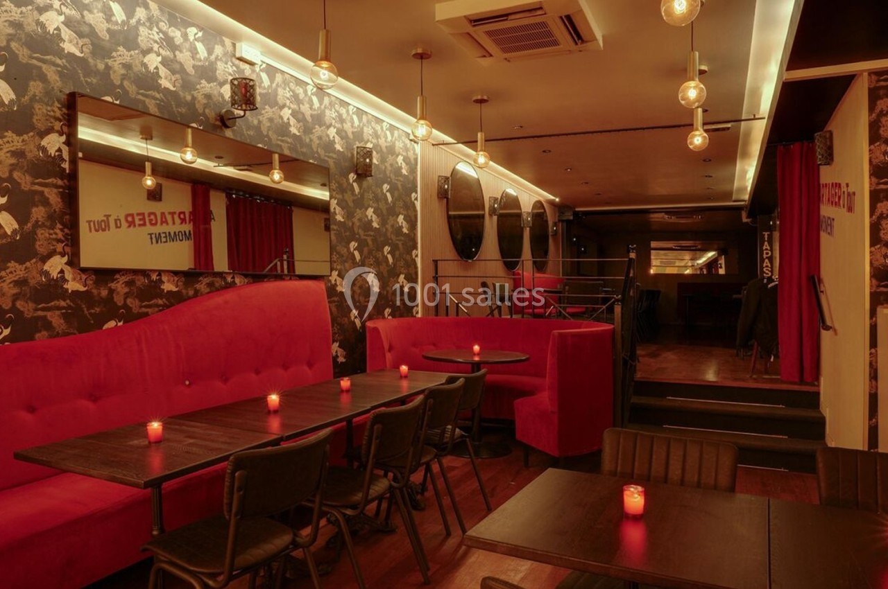 Salle de restaurant chaleureuse avec banquettes rouges, tables en bois sombre et éclairage tamisé par des bougies.
