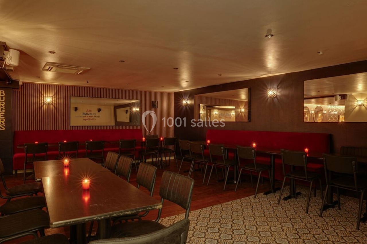 Salle de restaurant avec tables en bois sombre, chaises noires, banquettes rouges et éclairage tamisé.