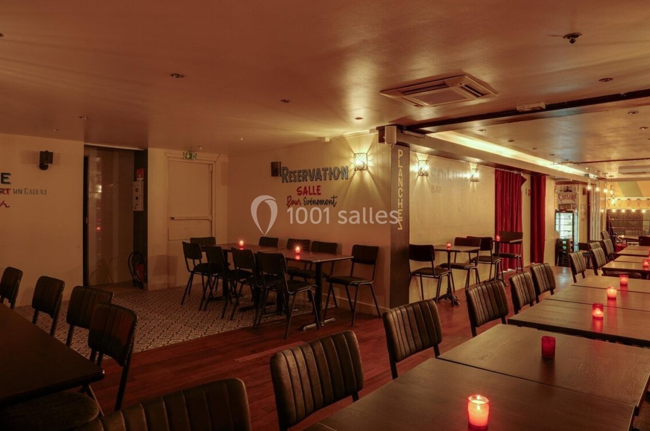 Salle de restaurant chaleureuse avec tables alignées, chaises noires et bougies rouges pour une ambiance intimiste.