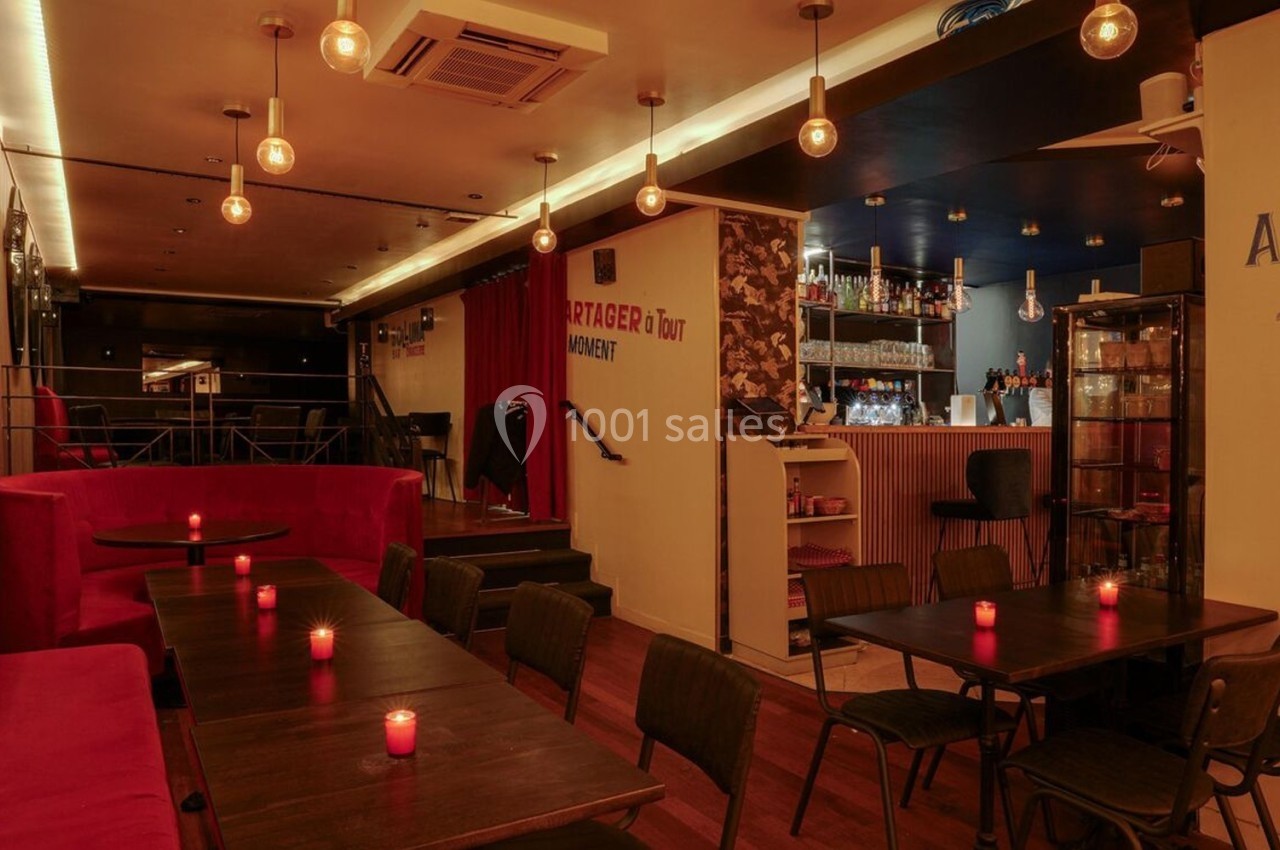 Salle de restaurant avec tables en bois, banquettes rouges, éclairage tamisé et bar en arrière-plan.