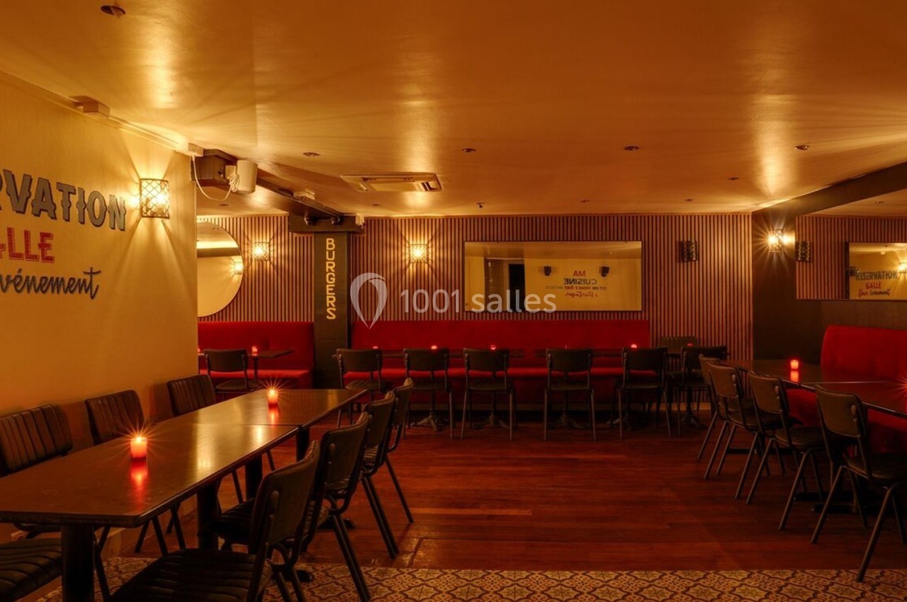 Salle de restaurant chaleureuse avec tables alignées, chaises noires, éclairage tamisé et décorations murales.