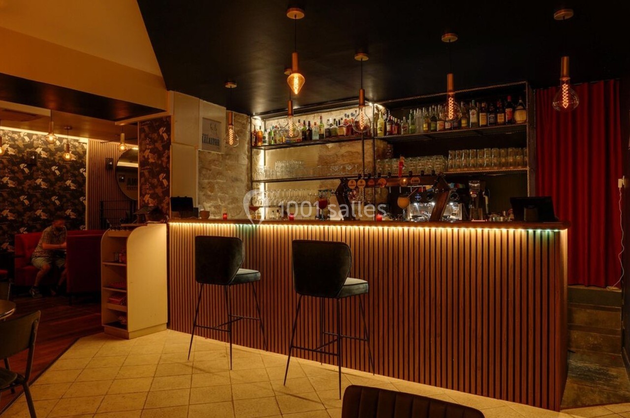 Bar chaleureux avec comptoir éclairé, tabourets hauts, étagères de bouteilles et ambiance tamisée.