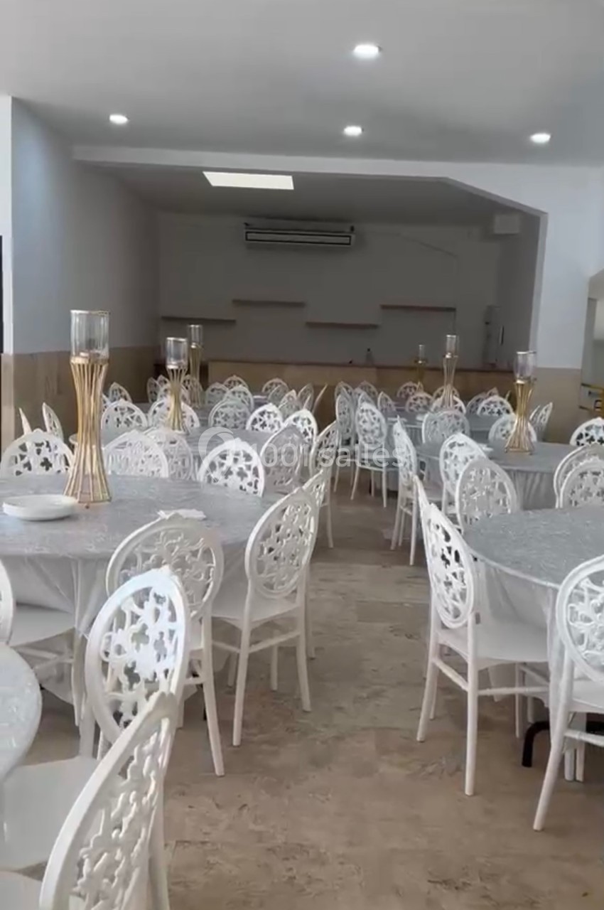 Salle lumineuse avec des tables rondes recouvertes de nappes grises et des chaises blanches décorées.