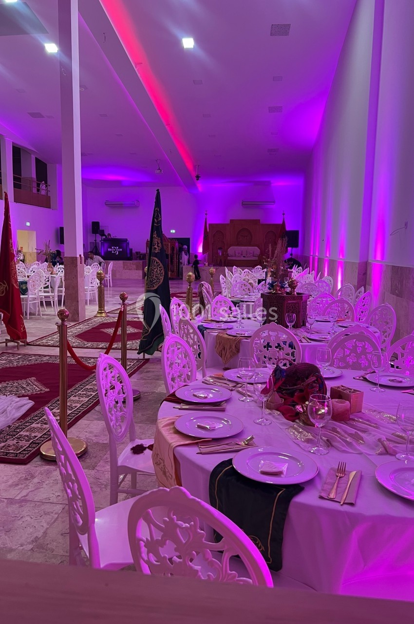 Salle de réception décorée avec des tables dressées, éclairage rose et éléments traditionnels en arrière-plan.