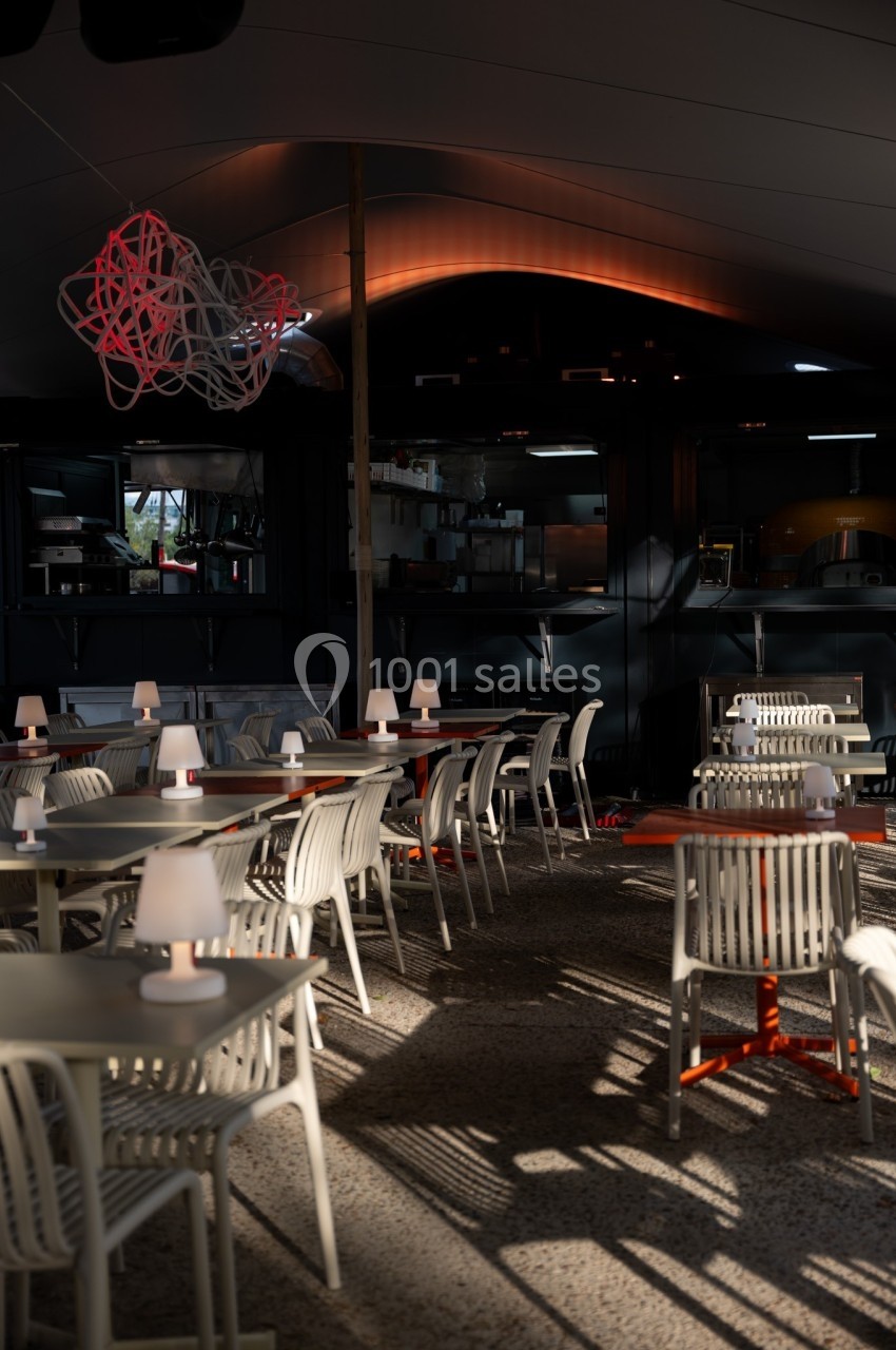 Salle de restaurant moderne avec des tables et chaises blanches, éclairée par une lumière tamisée en fin de journée.