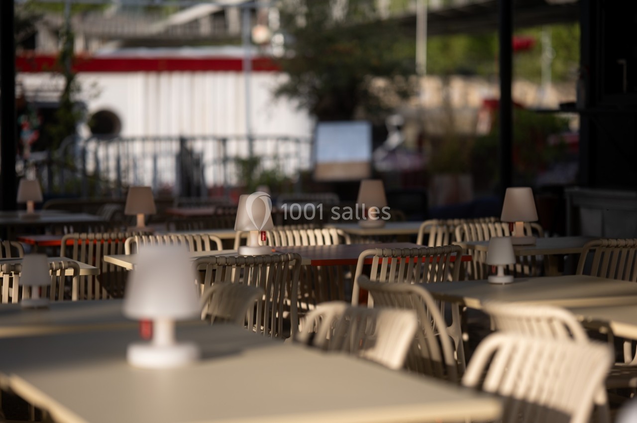 Terrasse d'un café avec des tables et des chaises vides, éclairées par des lampes de table en plein jour.