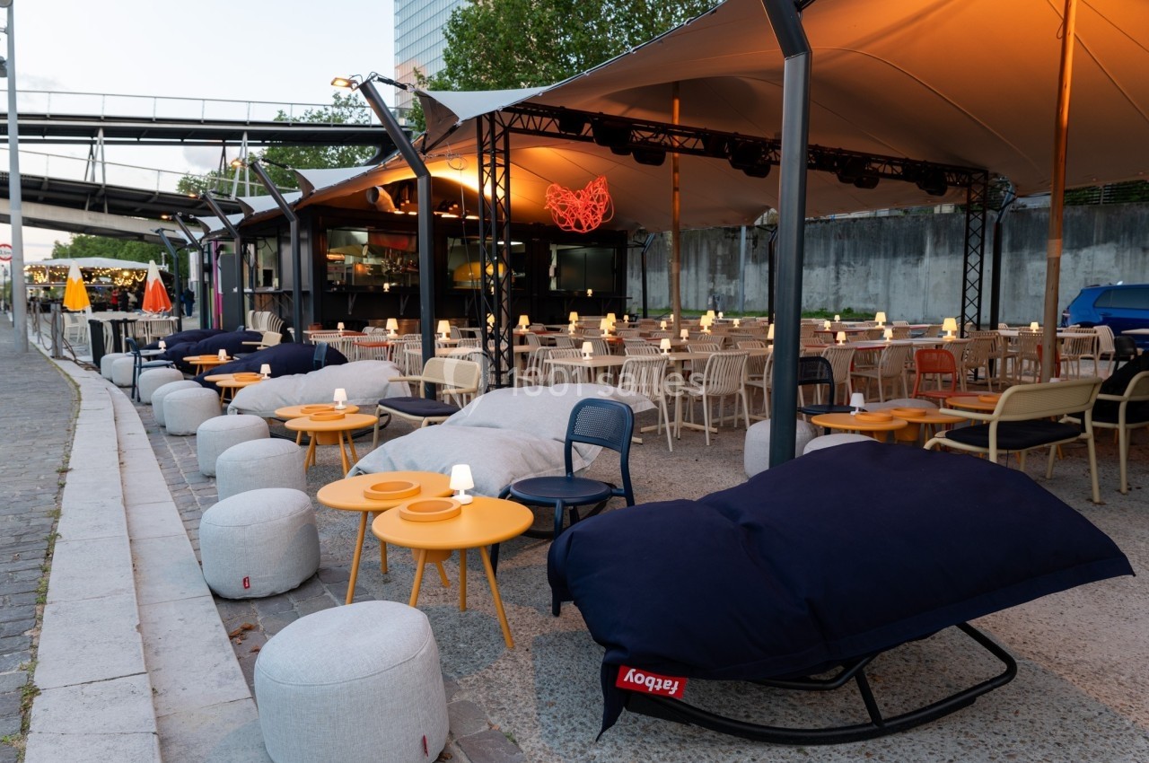 Terrasse extérieure aménagée avec poufs, tables basses et éclairage chaleureux sous une structure couverte.