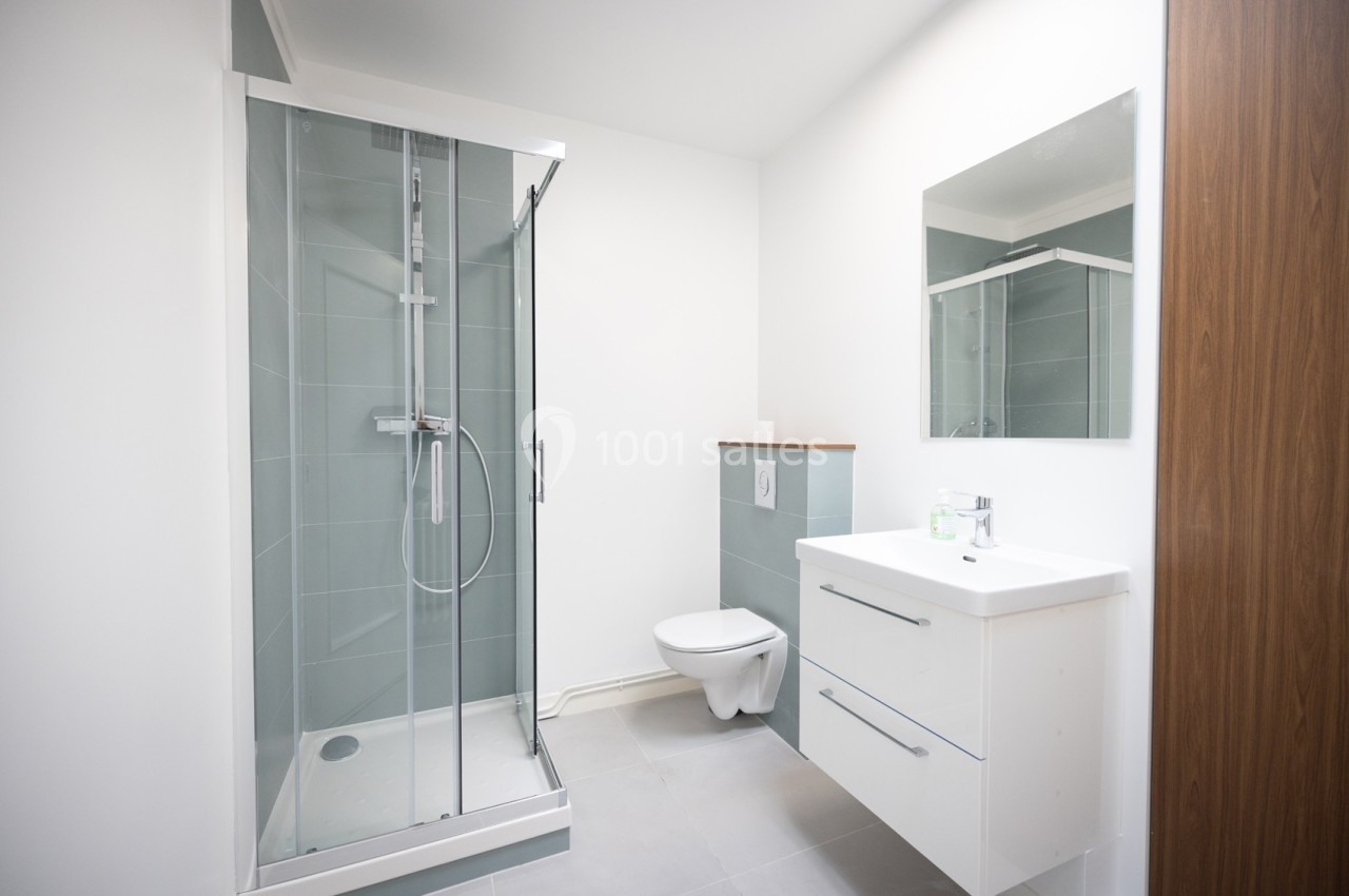 Salle de bain moderne avec douche vitrée, meuble vasque blanc, miroir et toilettes suspendues.
