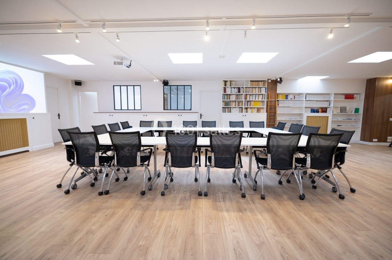 Salle de réunion lumineuse avec une grande table rectangulaire entourée de chaises noires et des étagères en arrière-plan.