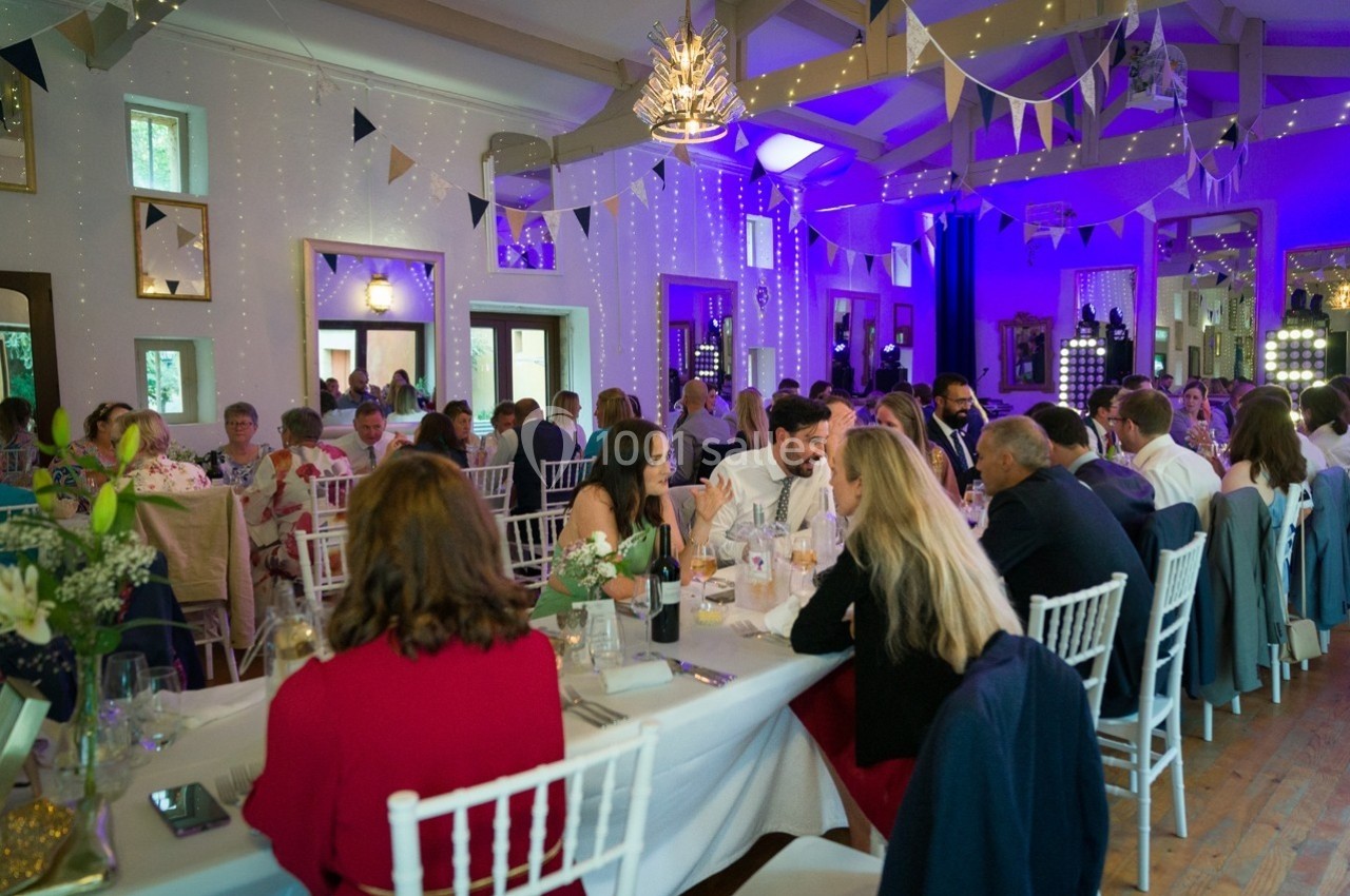 Salle décorée pour un événement, avec des invités assis à des tables, des guirlandes et un éclairage coloré.