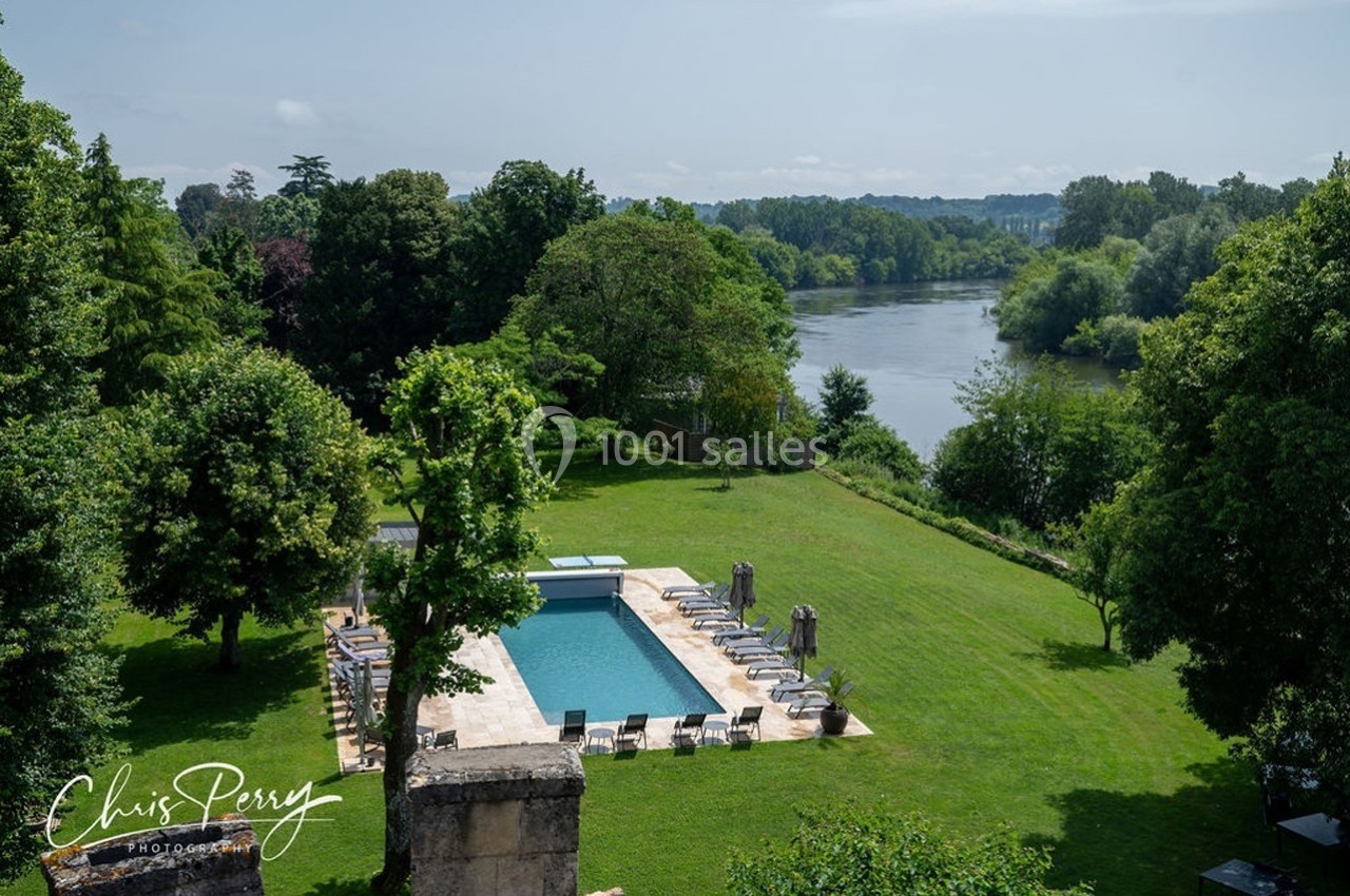 Vue d'un jardin verdoyant avec une piscine entourée de chaises longues, près d'une rivière bordée d'arbres.