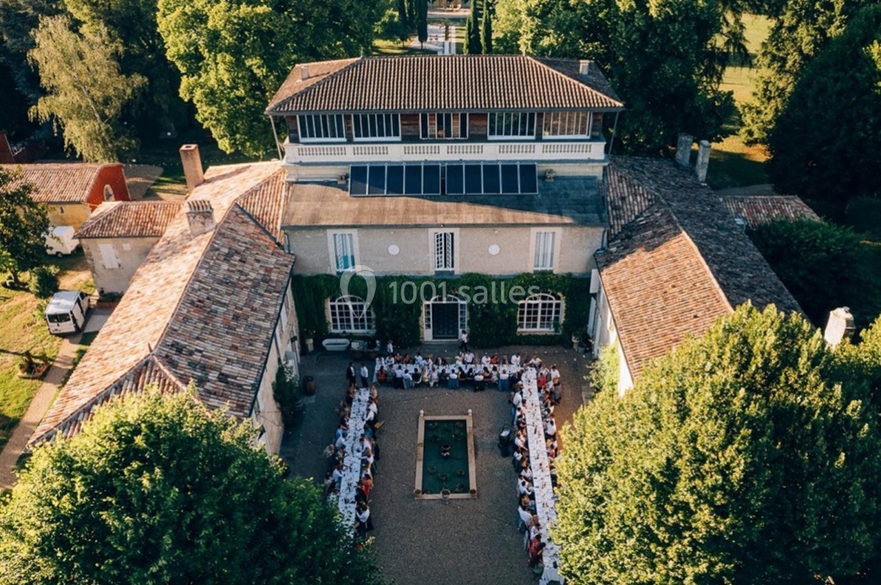 Vue aérienne d'un grand bâtiment entouré de verdure, avec des tables dressées en extérieur pour un repas collectif.