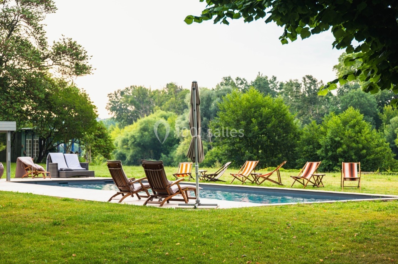 Chaises longues disposées autour d'une piscine extérieure dans un jardin verdoyant, par une journée ensoleillée.