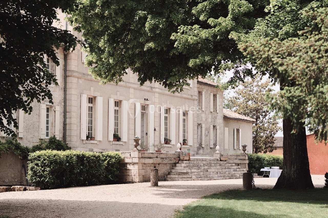 Façade d'un bâtiment en pierre entouré d'arbres, avec une allée gravillonnée et des marches menant à l'entrée.