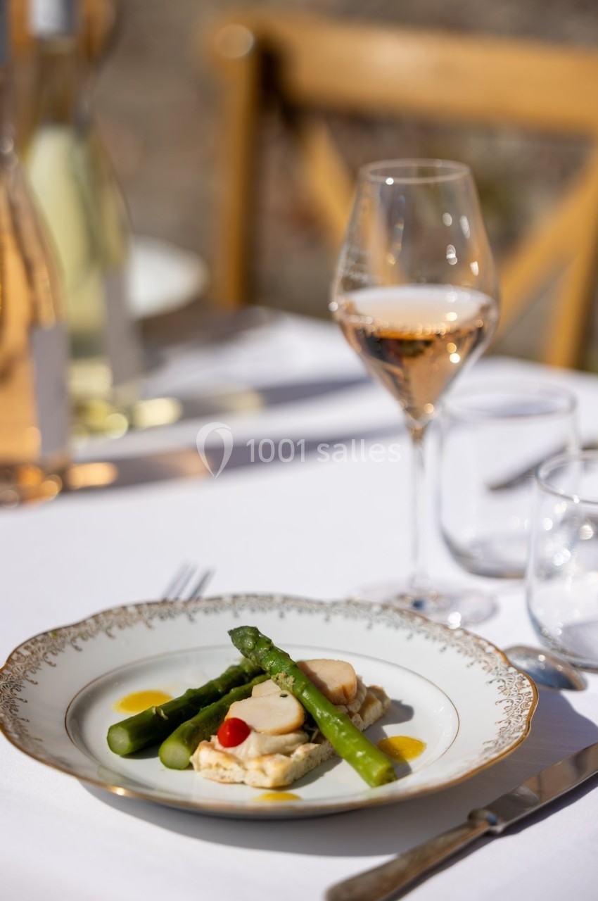 Assiette élégante avec asperges, poisson et sauce, servie sur une table dressée en extérieur avec un verre de vin rosé.