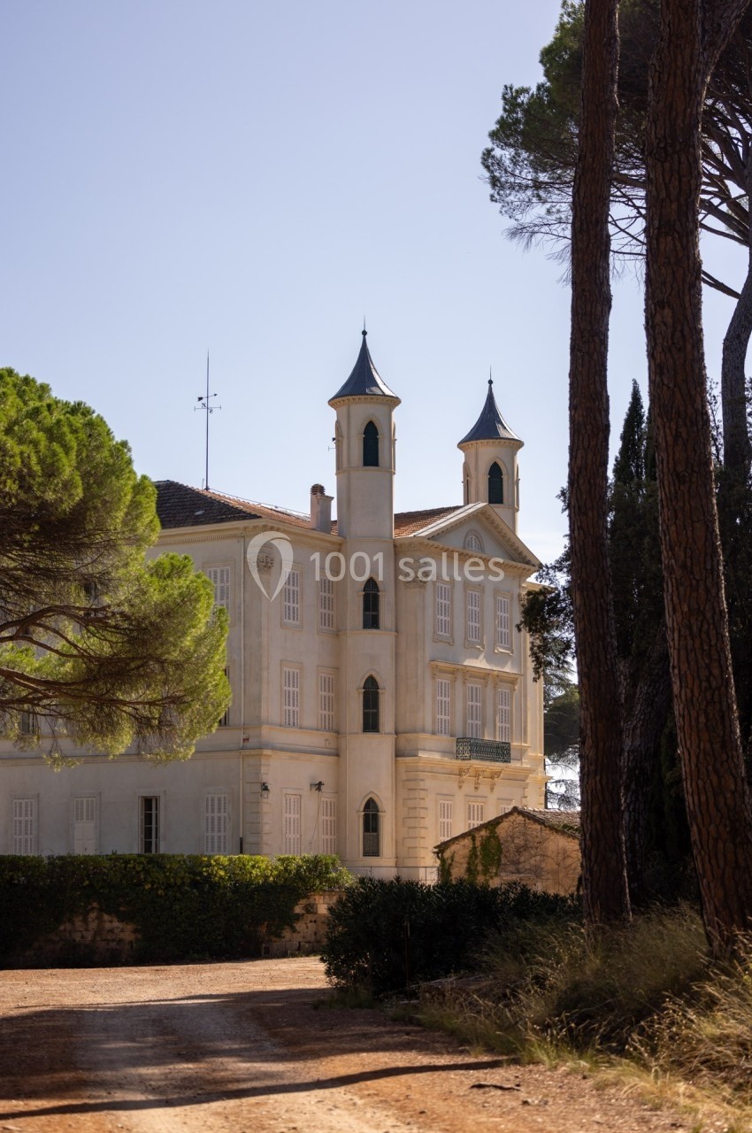 Façade d'un bâtiment ancien avec deux tours, entouré d'arbres et baigné par une lumière naturelle.