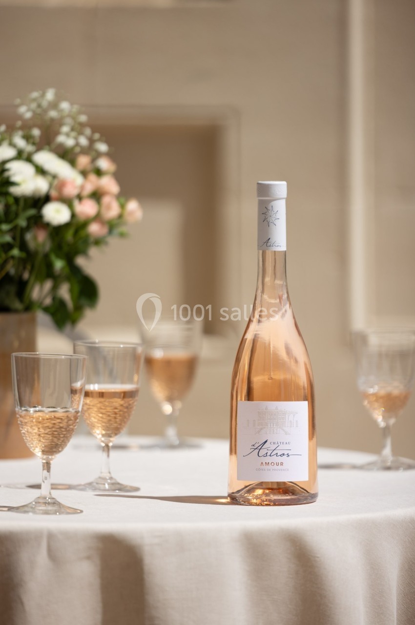 Bouteille de vin rosé posée sur une table avec des verres remplis, en arrière-plan un bouquet de fleurs.