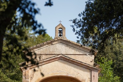 Petite chapelle ancienne entourée de végétation, avec une façade simple et un clocher surmonté d'une croix.