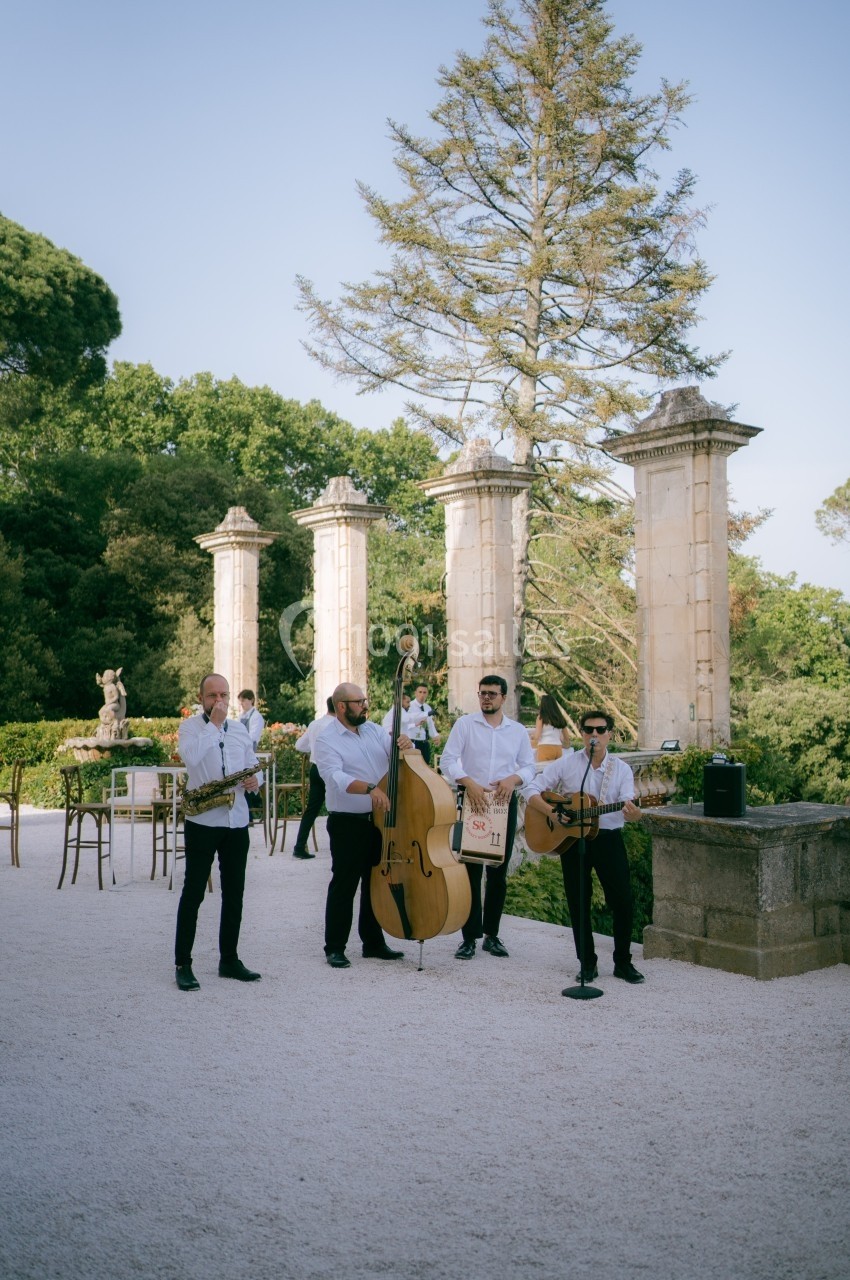Un groupe de musiciens joue en plein air devant des colonnes anciennes, entouré de verdure.