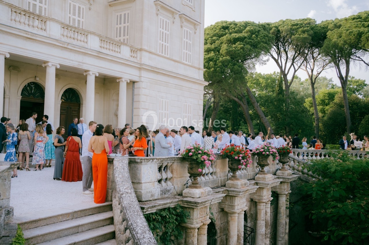 Groupe de personnes rassemblées sur une terrasse élégante devant un bâtiment historique entouré de verdure.