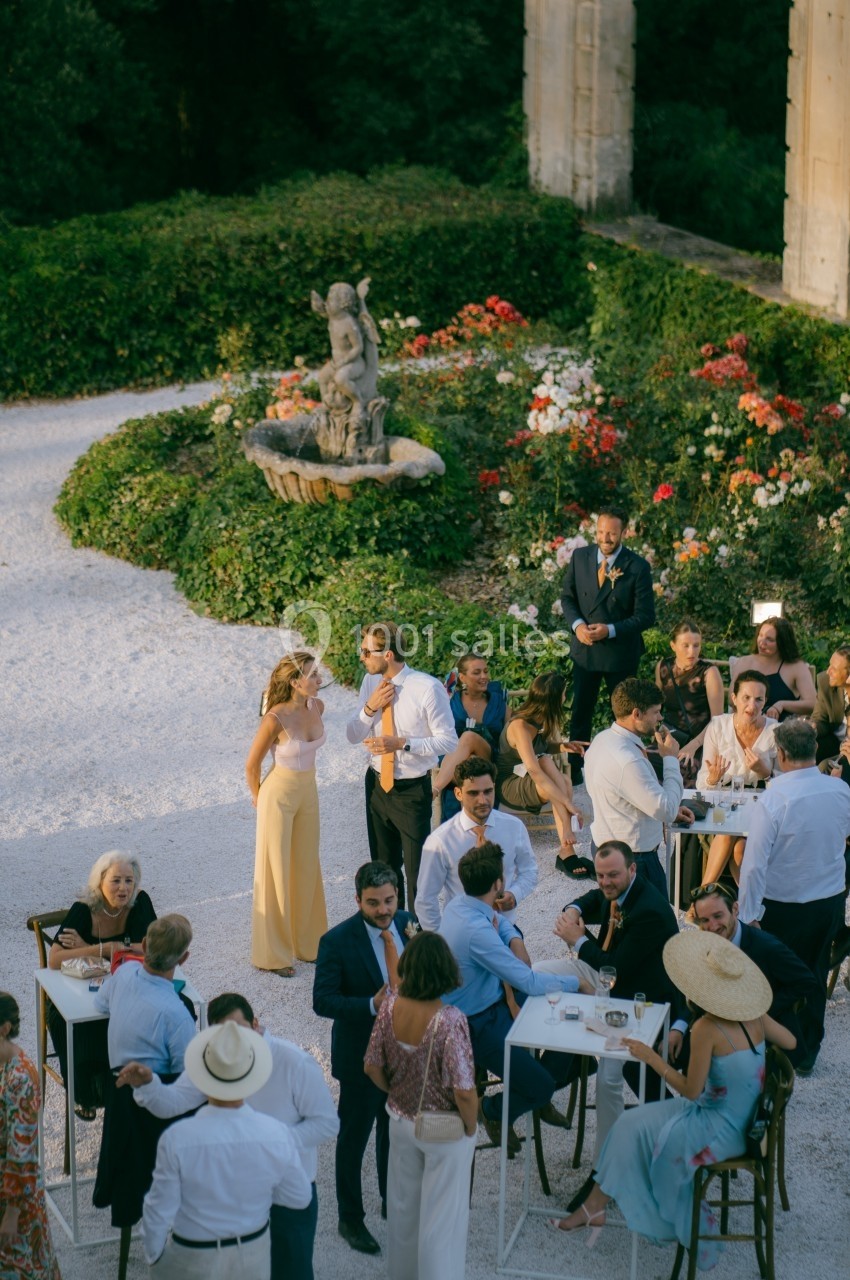 Groupe de personnes discutant et partageant un moment convivial dans un jardin avec une statue et des fleurs en arrière-plan.