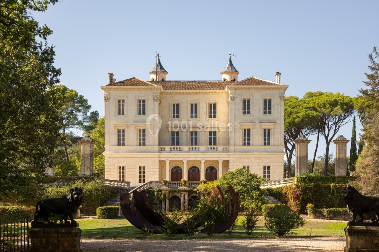Façade d'un château entouré de jardins, avec sculptures et arbres sous un ciel dégagé.