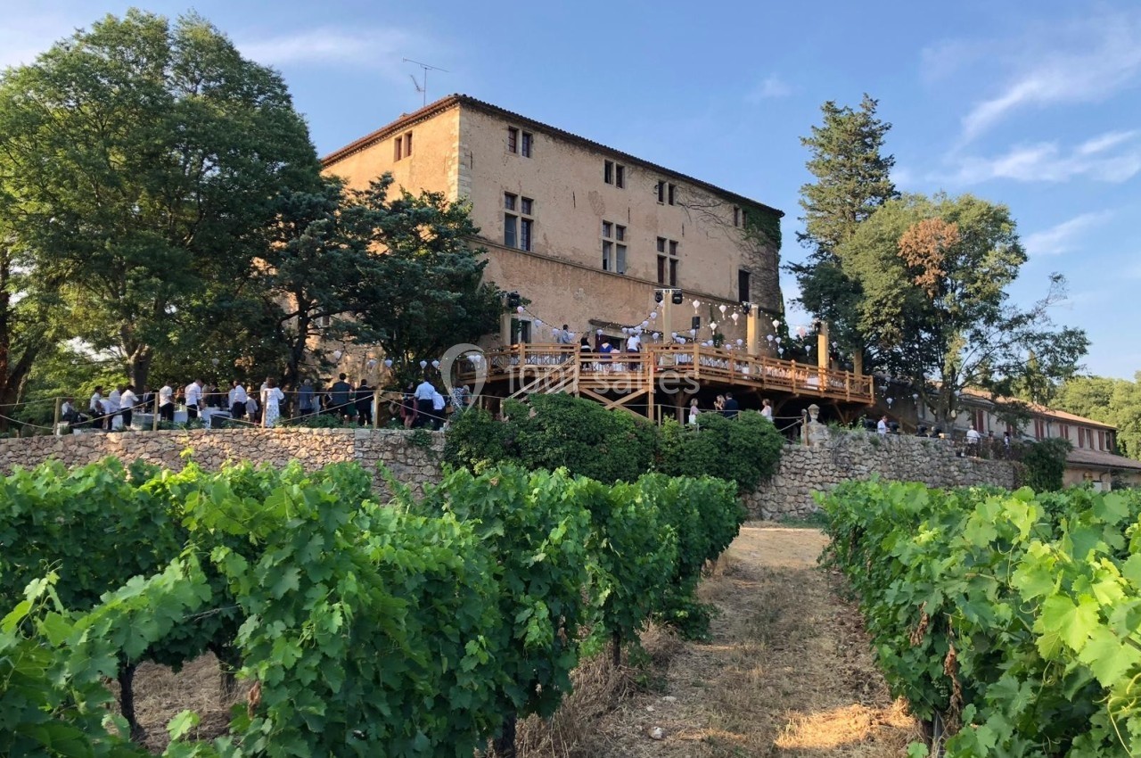 Un bâtiment ancien en pierre entouré de vignes, avec une terrasse en bois animée par des convives.